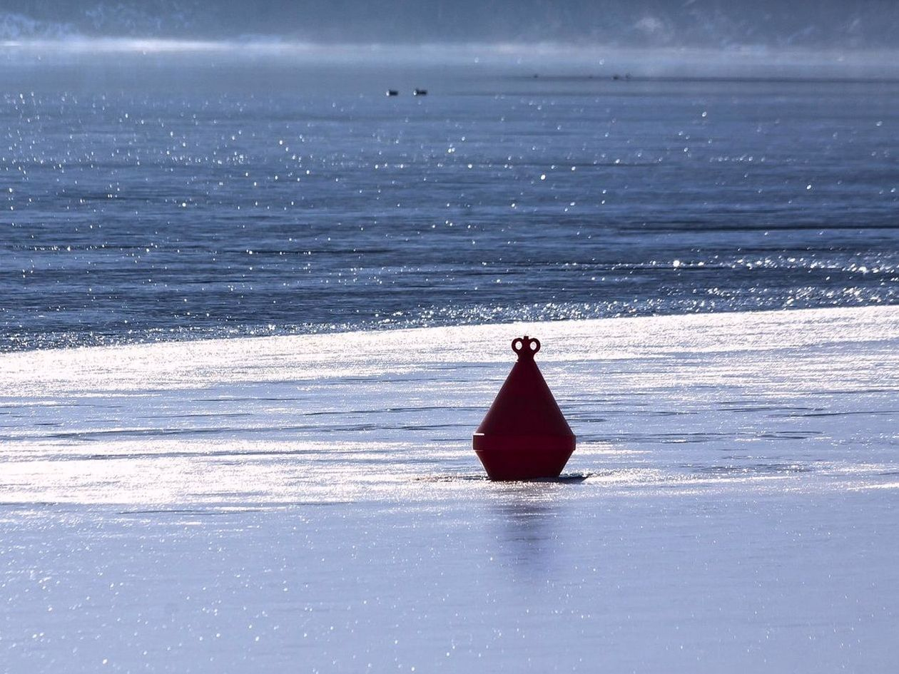 Un cuaderno gastado y lápiz sobre hielo mojado, junto a un agujero de pesca